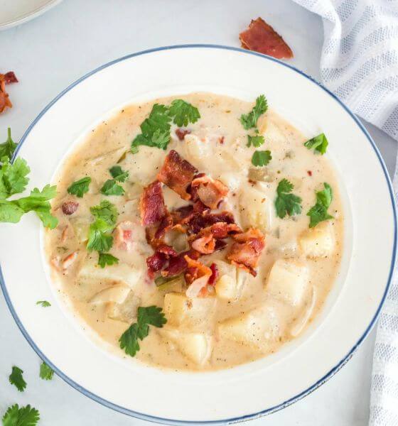 crockpot potato soup in white bowl with bacon on top