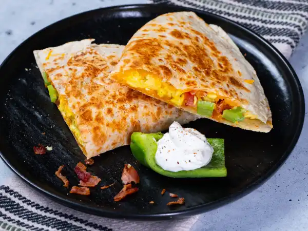 2 36 - ¡Hazte a un lado, burritos de desayuno! ¡Las quesadillas AM están aquí para revitalizar la mañana Tex-Mex! Las tortillas doradas y crujientes envuelven huevos esponjosos, queso derretido y pimientos verdes brillantes con el fantástico crujido del tocino desmenuzado... ¡eso sí que es celestial! Lleva las quesadillas AM contigo para despertarte rápido pero contundente o disfrútalas cómodamente con un poco de crema agria... ¡de cualquier manera, la mañana es tuya!