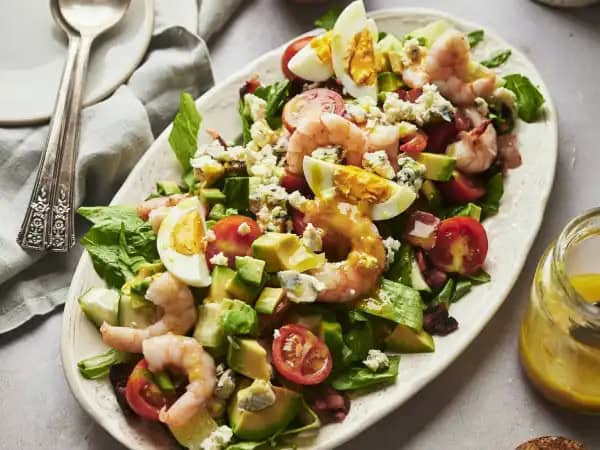 image 10348 - Sally eats shellfish salad by the seashore. Even if your name isn't Sally, Shrimp Cobb Salad will have you reciting poetry — that's how good this dish tastes! Your tongue will get all twisted up by the extravagant flavors... savory shrimp, juicy cherry tomatoes, crunchy cucumbers, hearty hard-boiled eggs, creamy avocado, succulent bacon, and extra-tangy crumbled blue cheese. When mixed with refreshing greens and a delicious Dijon mustard vinaigrette, you're sure to be sold on all of the crazy-good bites found in Shrimp Cobb Salad. Sea?! Sally knows you will love it! (Ha)