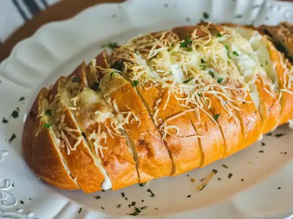 image 16120 - Is there anyone on the planet that doesn't love an herby, butter-ladened, and crusty French bread roll smooshed together with a variety of ooey-gooey, yummy melted cheeses?! Yeah, we didn't think so! You can't go wrong with this Hasselback Cheesy Bread whether you are feeding a crowd, or, um, not a crowd (we won't tell). Did we mention the melted cheeses? Like three different kinds of melted cheeses? Ah, amazing mozzarella, plus some classic white cheddar, and the perfectly-sharp parmesan, all of which create a match truly made in toasty French bread heaven! Make Hasselback Cheesy Bread anytime your crowd (or just you) craves some magnificently melodious melted cheese.