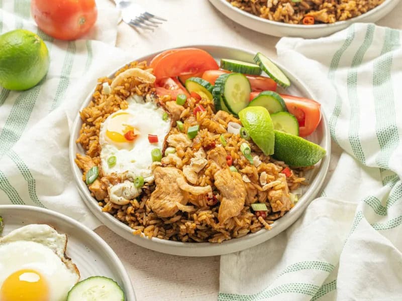 image 19019 - One of the national dishes of Indonesia, Nasi Goreng, takes fried rice to new and delicious places. Infused with savory flavors from the soy sauce and shrimp paste and loaded with juicy chicken, Nasi Goreng is nourishing and incredibly gratifying to eat! Topped with a fried egg and fresh vegetables, this dish has everything you could want from fried rice and more! Plus, it only takes 20 minutes to make, so you'll never need to worry about bland fried rice again!