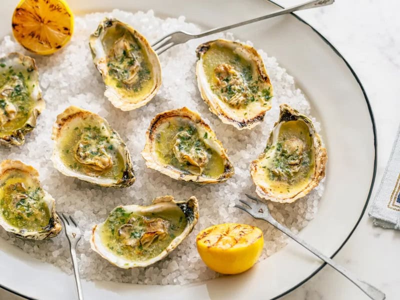 image 21817 - When you think of oysters on the half shell, you imagine them chilled, served on a bed of ice with some cocktail sauce alongside. That's all well and tasty, but it's not the only way to serve these juicy, salty treats. Boozy Grilled Oysters top each oyster with a heaping helping of fragrant, sparkling, herbaceous compound butter and grill them until they are bubbly and melty. These savory shots of flavor are sure to get the party feeling fun and free! You'll be reaching for more Boozy Grilled Oysters throughout the rest of the celebration, so make sure you make enough!