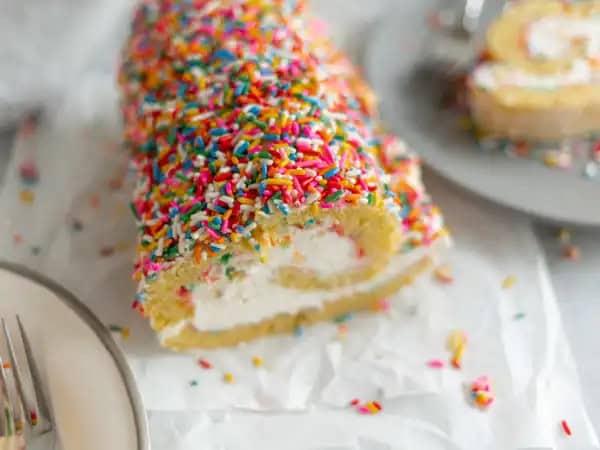 image 8942 - Well, this will certainly get the party on a roll! Birthday Cake Roll takes inspiration from Swiss rolls for a spiral of sweetness that will make anyone's celebration a blast! The cake is colorfully speckled and tender, with a creamy, tangy cream cheese frosting inside the swirls! A smooth white chocolate ganache on top helps to take this dessert from novelty to new favorite! Birthday Cake Roll will be sharing in the festivities with you for a long time to come!