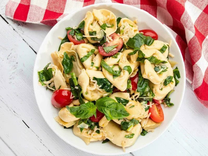 image 247 318 - When the weather is just right, being outside at all times of the day is a must—meal times included! The Ultimate Picnic Salad is the perfect go-to when you want to whip something up quickly and not miss a minute of the glorious sunshine. With every bite, you'll enjoy some cheesy tortelloni, a mix of crunchy fresh greens, juicy ​​tomatoes, bitter artichokes, and salty parmesan cheese. It's all tossed together in a sweet and savory dressing that will make your day even brighter! Grab your favorite ice-cold summery drink and a quilt and enjoy the Ultimate Picnic Salad!